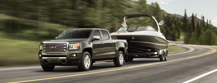 Image of the 2017 GMC Canyon small pickup truck towing a speed boat in motion down a mountainous road.